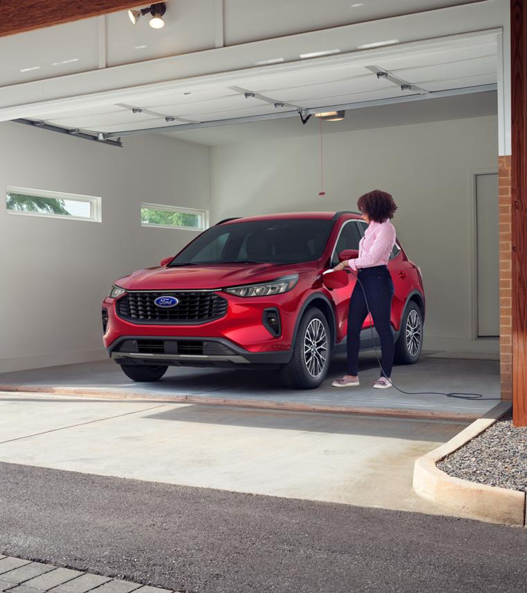 2025 Ford Escape® SUV Plug-In Hybrid model being plugged in by a woman in a garage