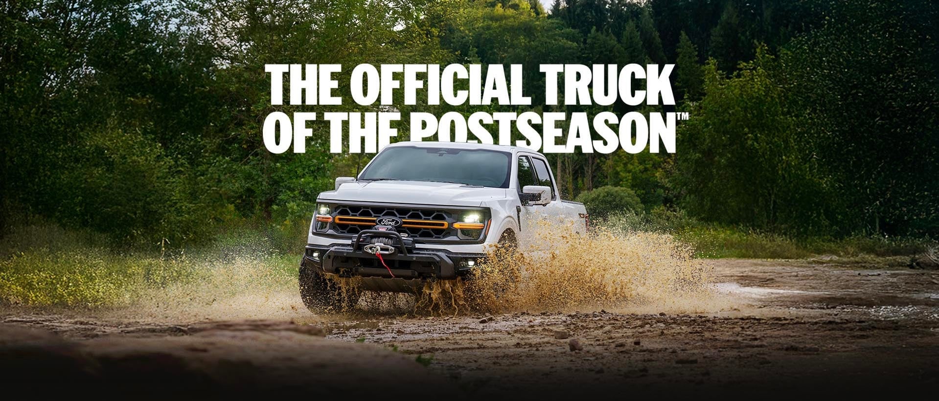 White 2026 Ford F-150® truck driving through a muddy puddle on an off-road forest trail