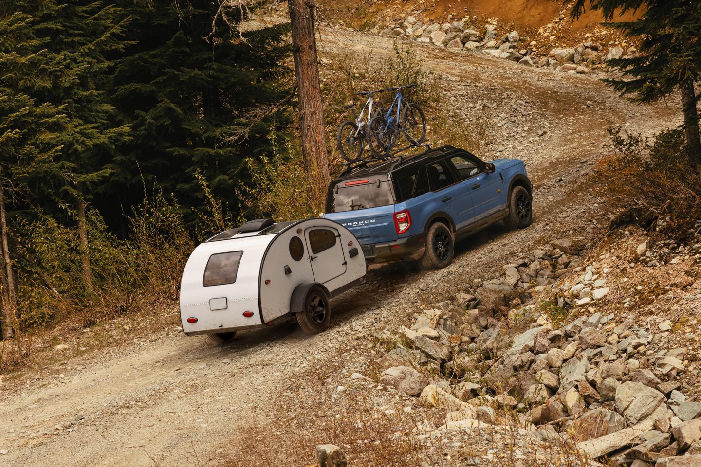A 2025 Ford Bronco Sport® Badlands® SUV driving up a rocky hill while towing a small camper trailer