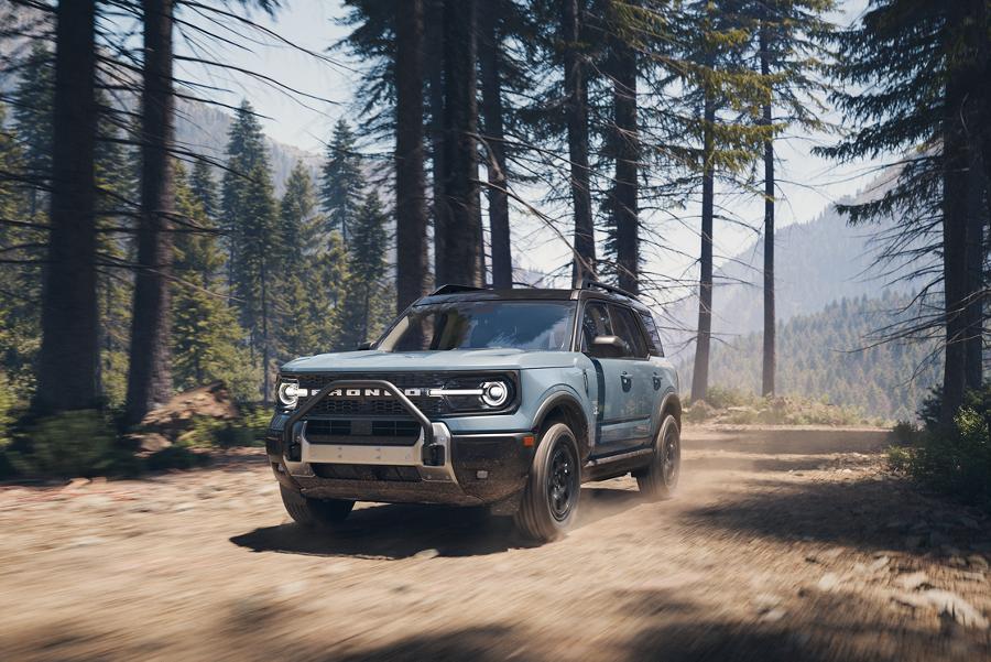 A Ford Bronco Sport driving on a dirt trail through a forest with tall pine trees