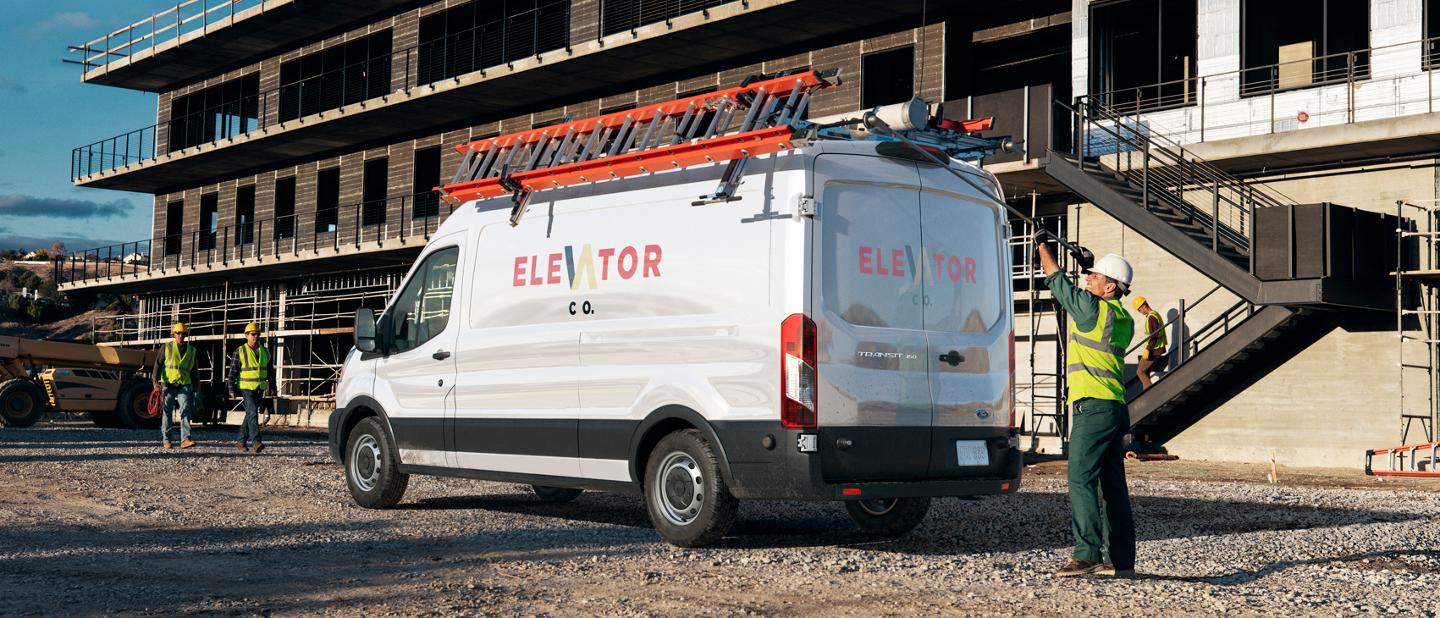 A 2025 Ford Transit® van parked at a construction site with a worker standing at the rear doors