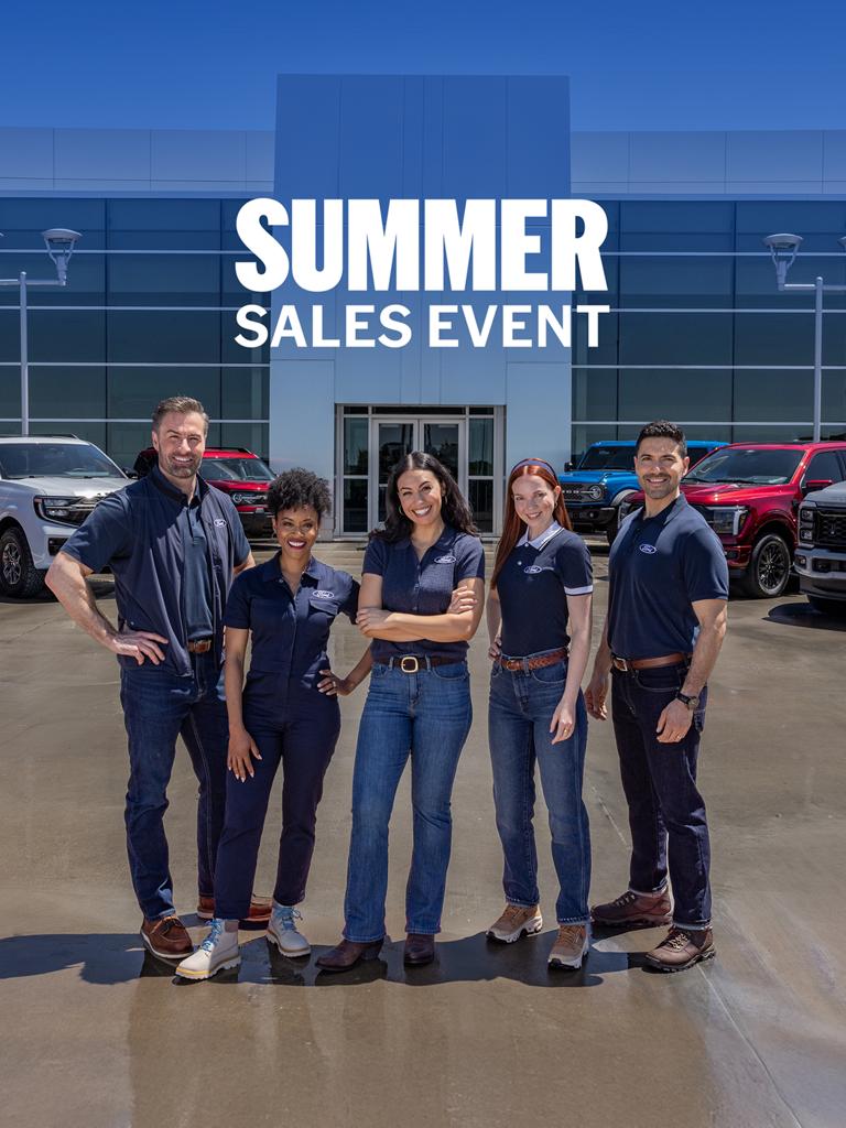 Group of employees standing in front of a Ford dealership