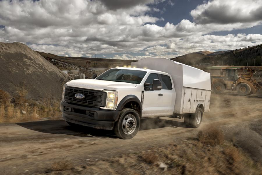 A 2025 Ford Super Duty® F-450® XL with a utility box being driven up a dirt road jobsite