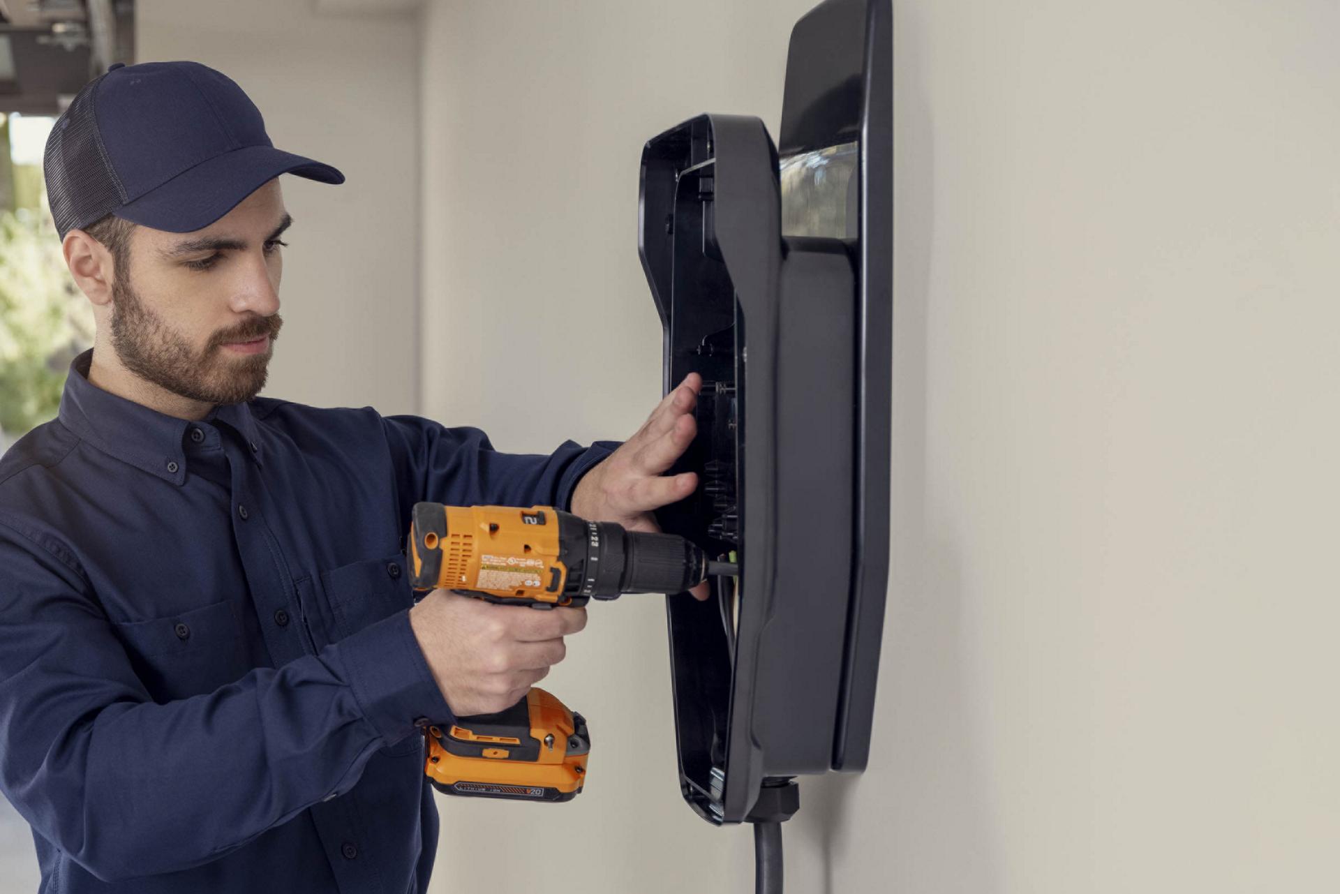 Technician using a power drill to install an electric vehicle home charging station on a wall