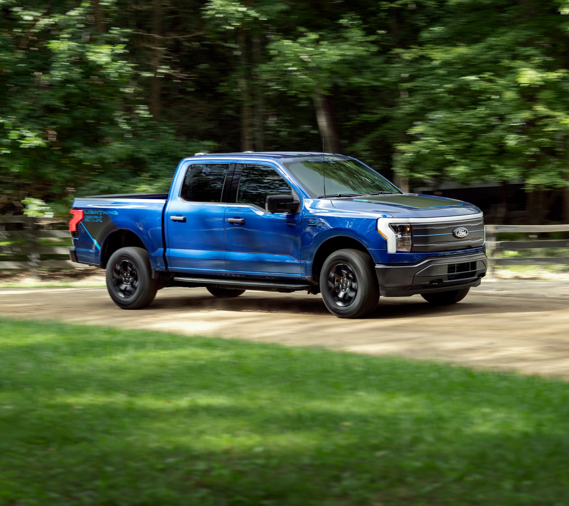 Ford F-150 Lightning truck driving down road next to grass
