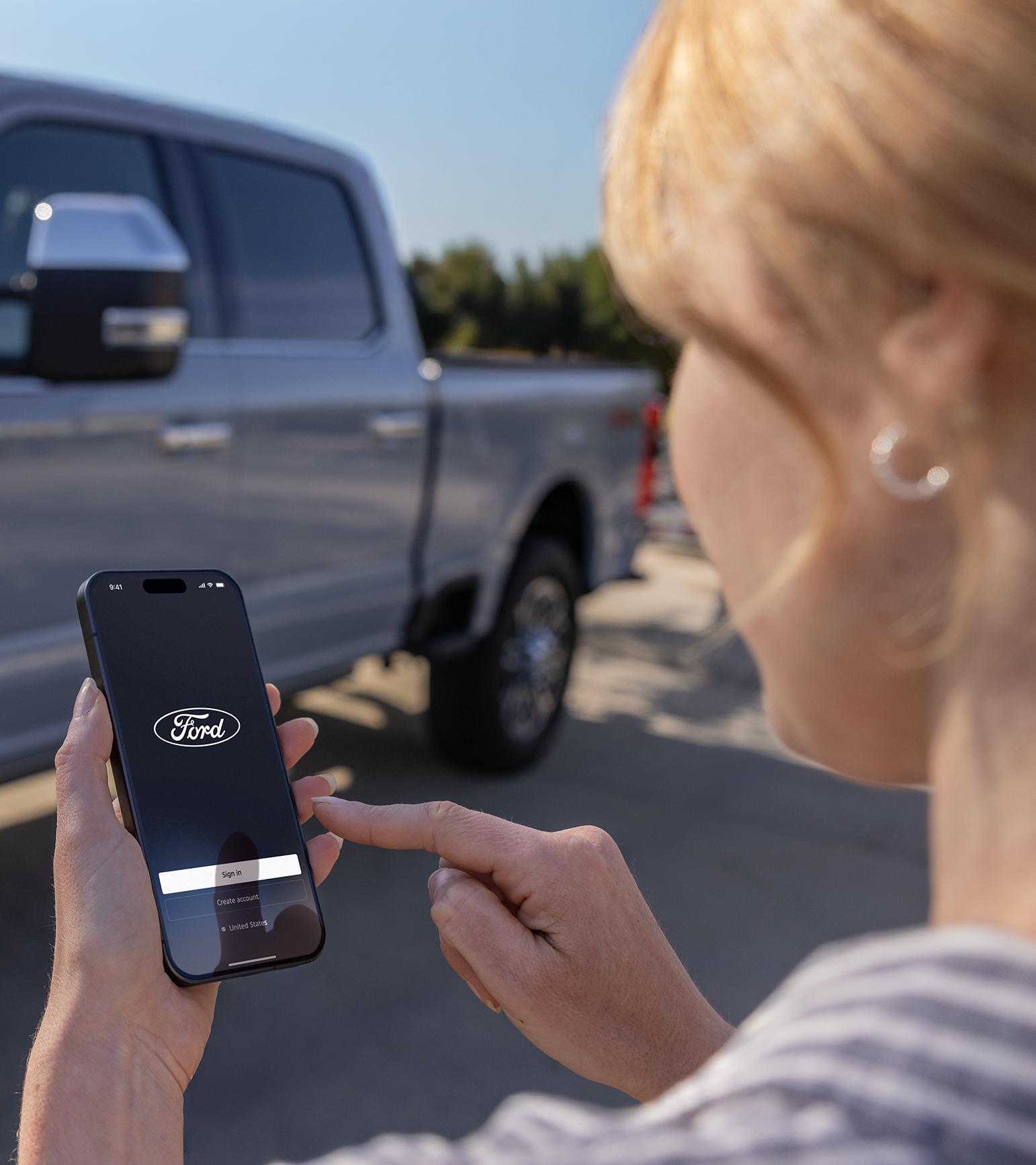 Woman opening the Ford app on her phone with a Ford truck in the background