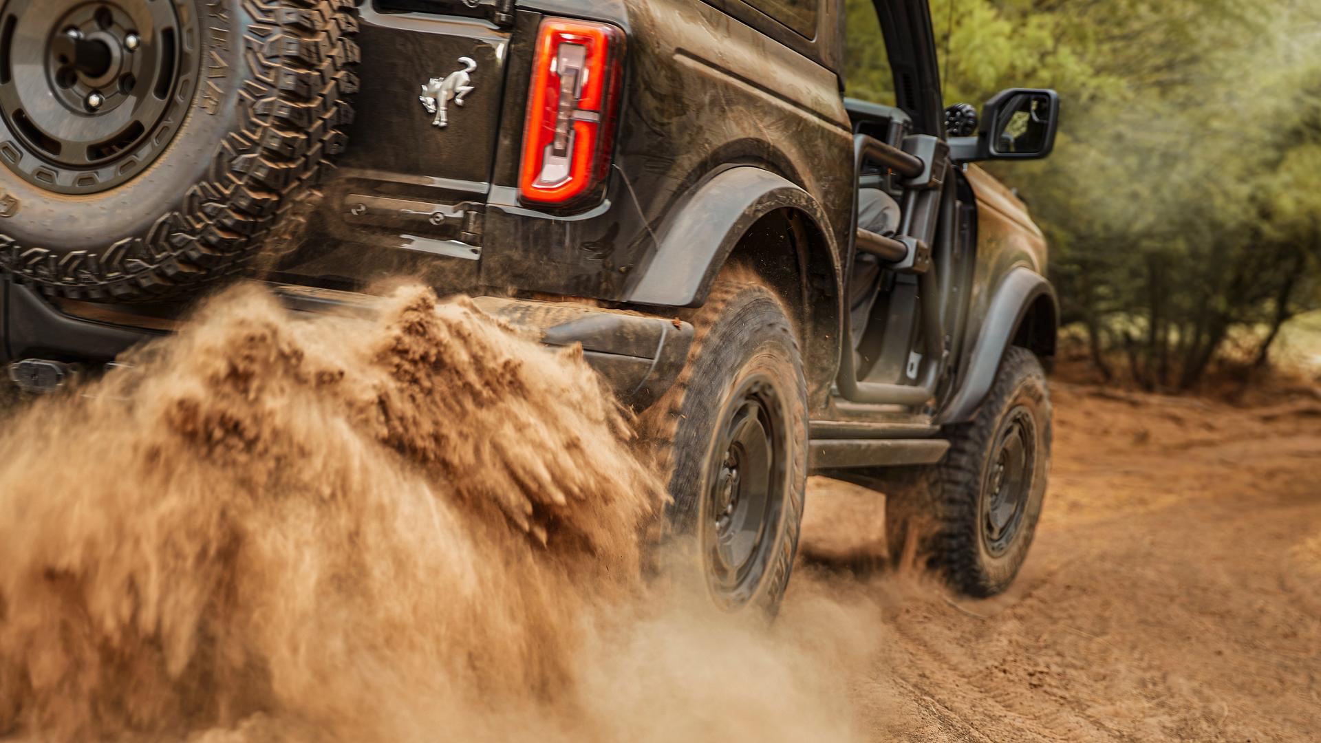 A 2026 Ford Bronco® SUV kicking up mud on a trail in the forest