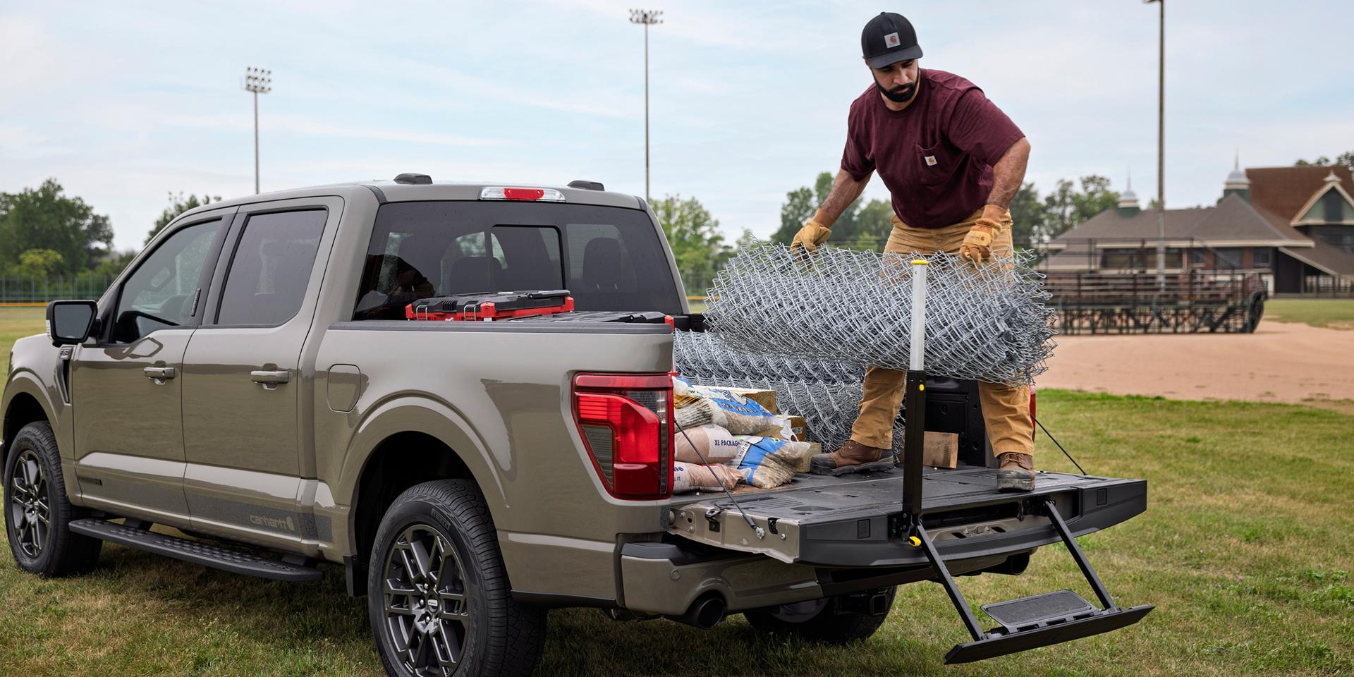 Man loading fencing into the bed of a 2027 Ford F-150® XLT model with the Carhartt® Package showing the tailgate step and assist bar