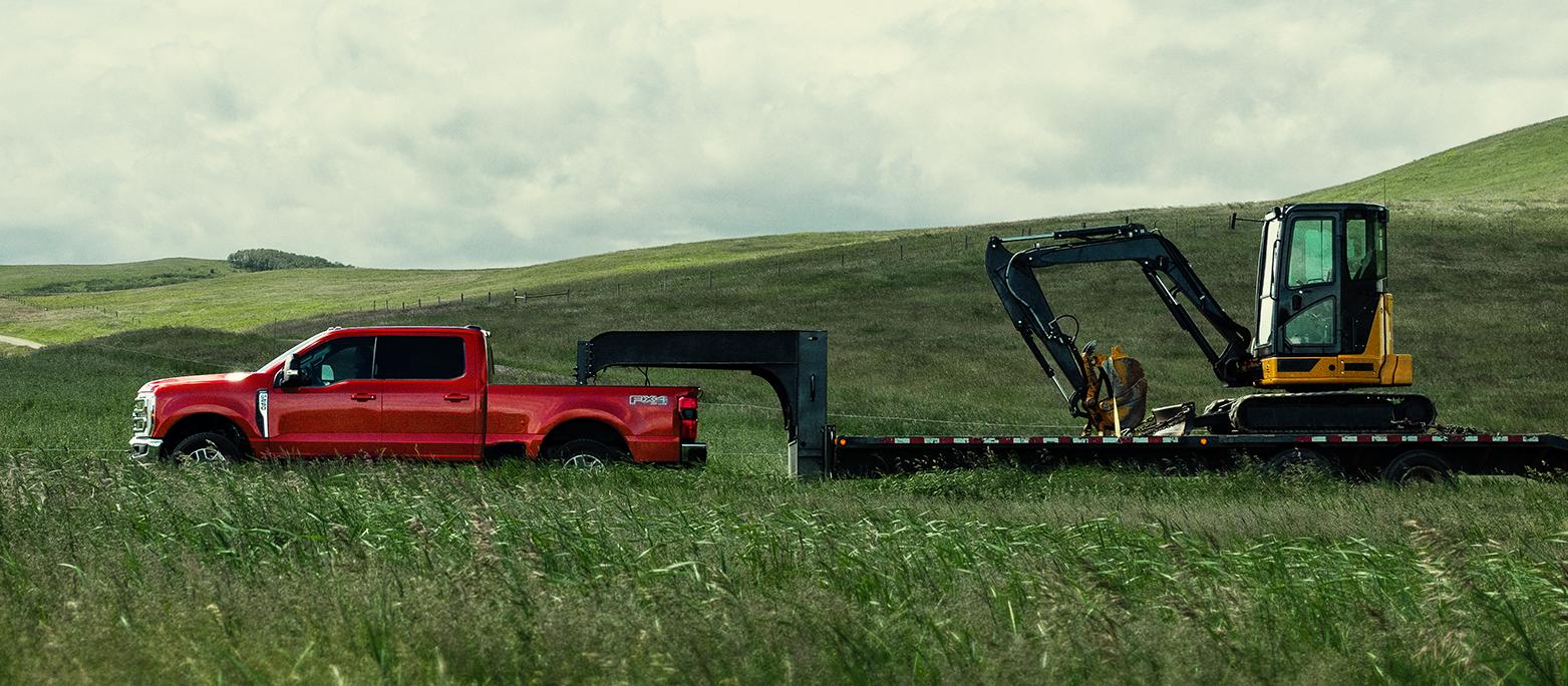 2027 Ford Super Duty® F-250® Lariat® model towing a large trailer of construction equipment through a grassy field