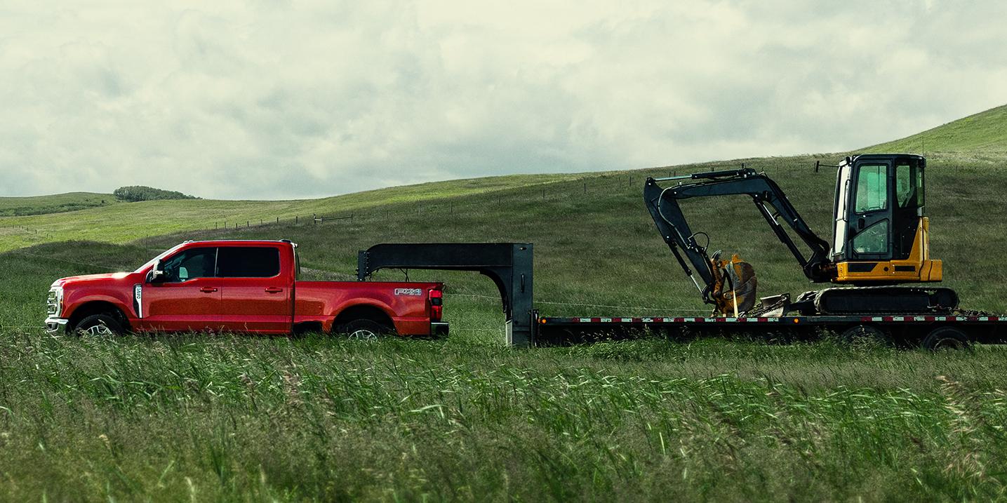 2027 Ford Super Duty® F-250® Lariat® model towing a large trailer of construction equipment through a grassy field