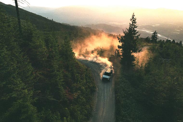 A 2026 Ford Bronco® SUV kicking up dust on a winding hillside trail at sunset
