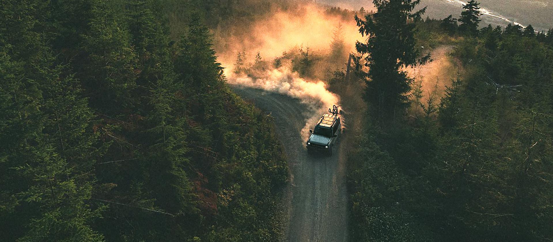 A 2026 Ford Bronco® SUV kicking up dust on a winding hillside trail at sunset
