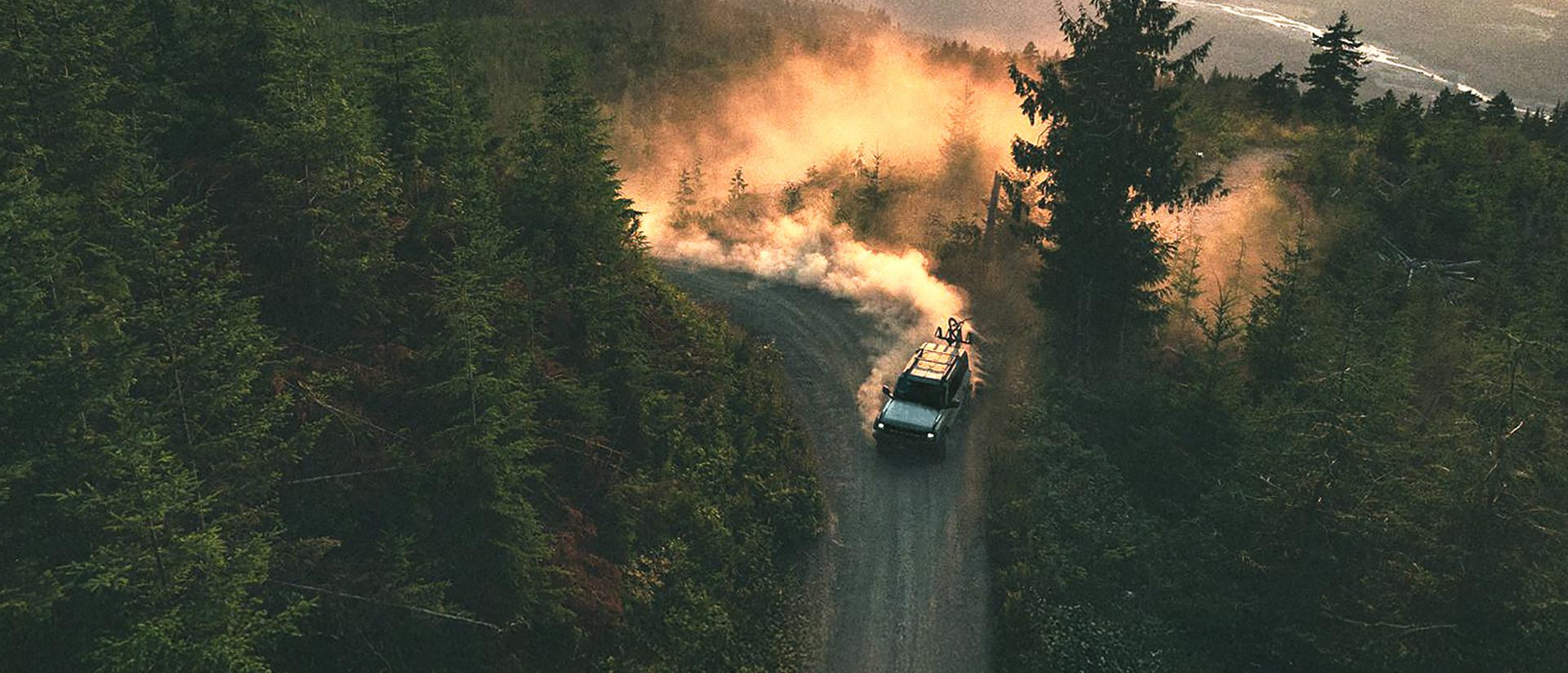A 2026 Ford Bronco® SUV kicking up dust on a winding hillside trail at sunset