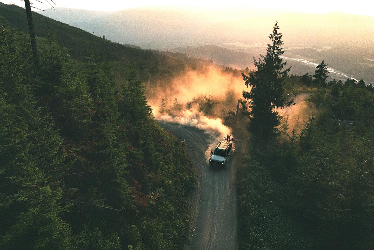 A 2026 Ford Bronco® SUV kicking up dust on a winding hillside trail at sunset