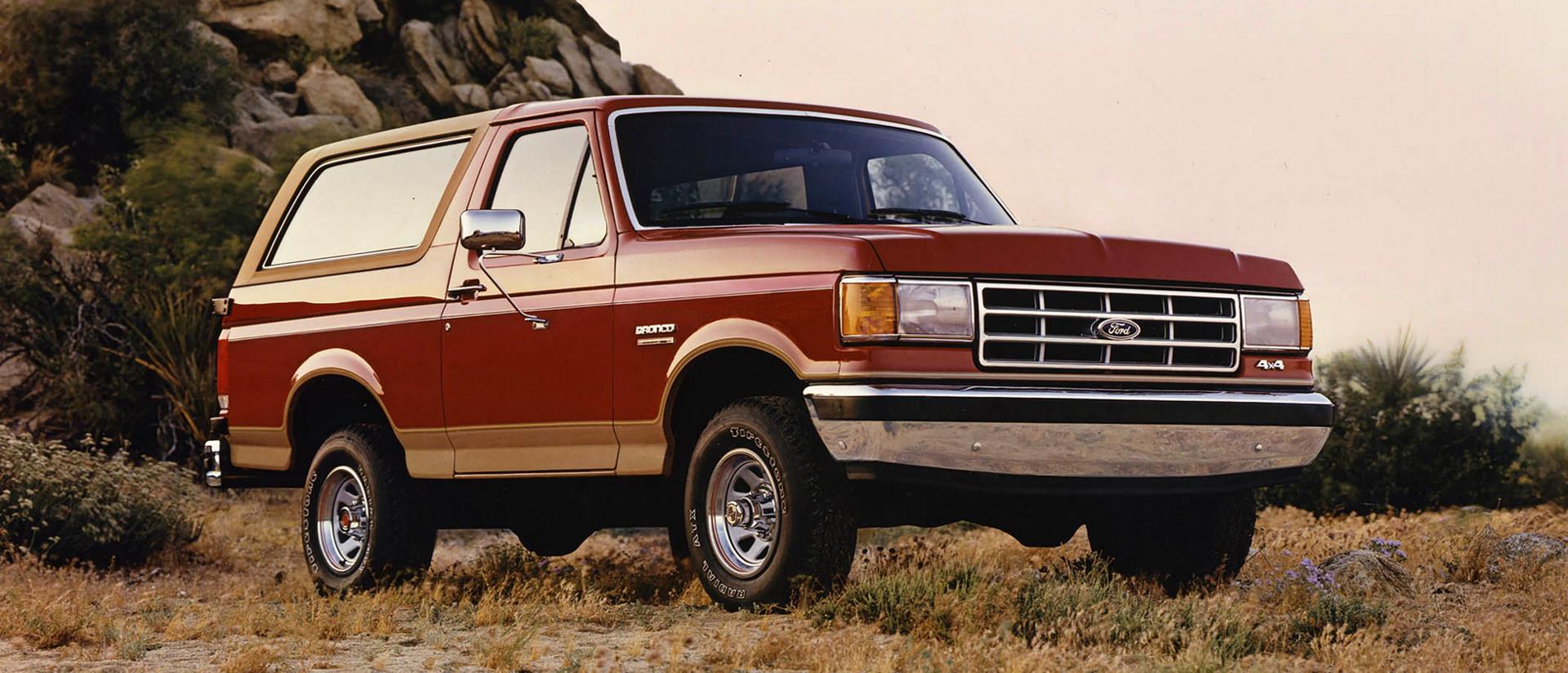 A vintage orange 1987 Ford Bronco® model parked in front of a rocky landscape