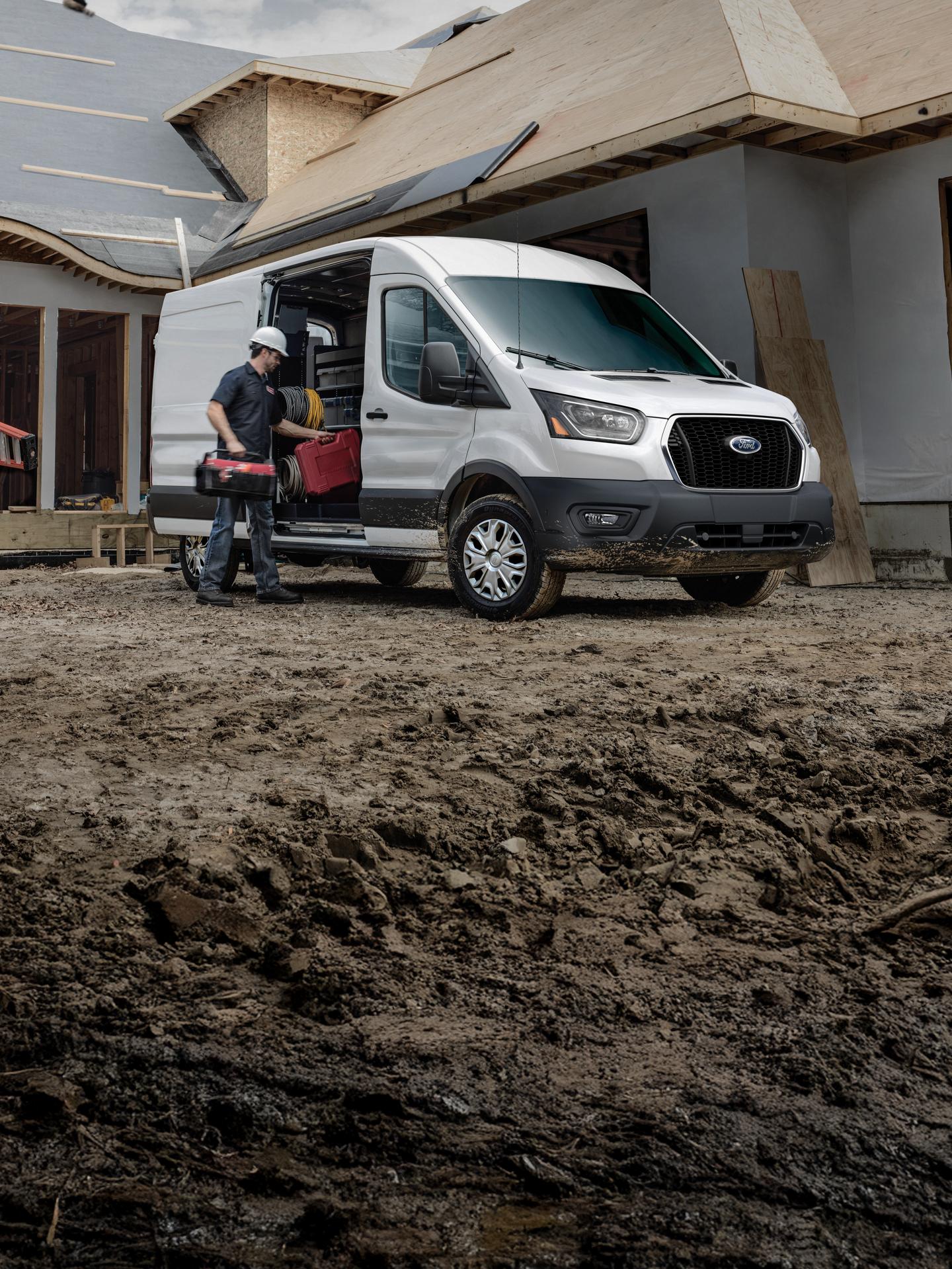 Imagen de una persona trades colocando herramientas en una white Transit Cargo Van en un sitio de construcción residencial.