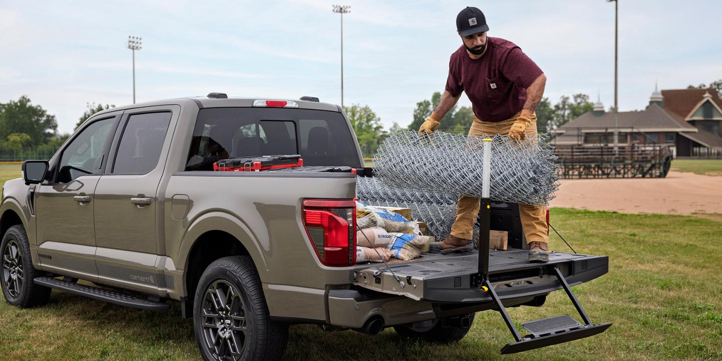 Man loading fencing onto a 2027 Ford F-150® XLT plus Carhartt® Package truck bed, including the tailgate step and assist bar