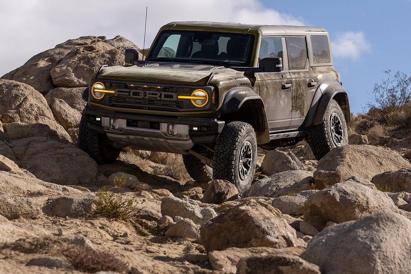 A white 2024 Ford Bronco® with "Bronco Off-Roadeo" branding on the side as it climbs a steep dirt trail, seen from the rear
