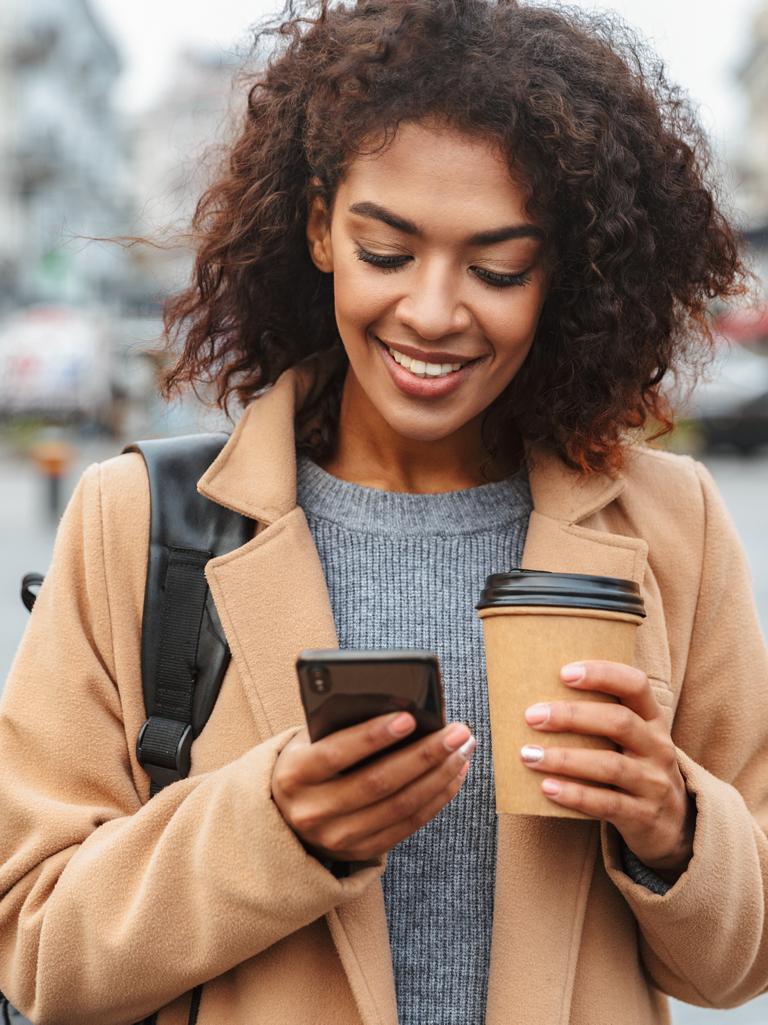 Person standing outside holding their smartphone in one hand and a coffee in the other