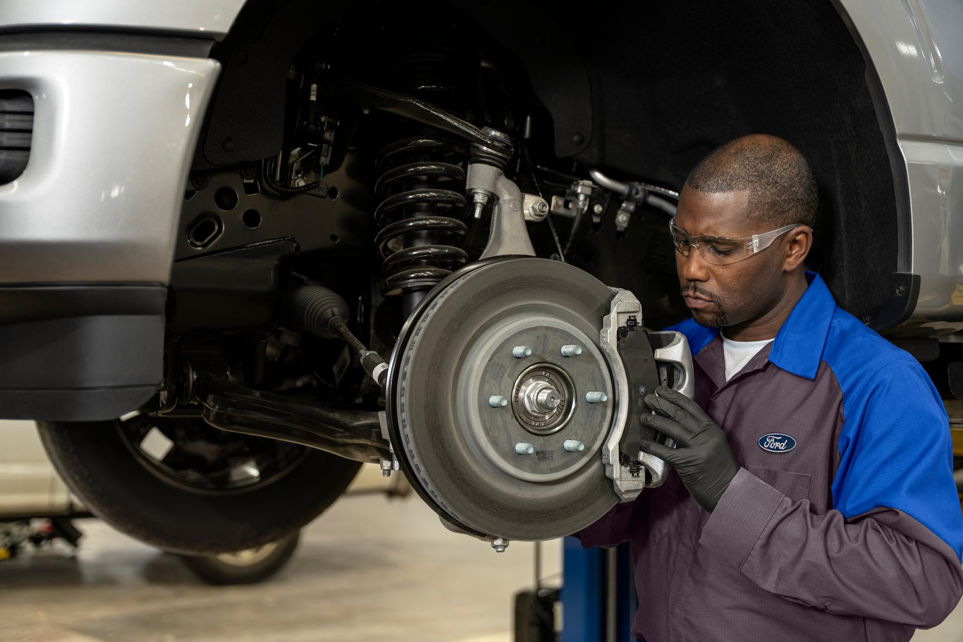A Ford Service technician inspects the brakes on a Ford vehicle