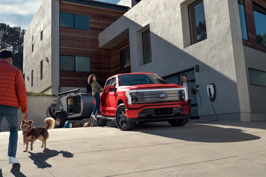 Woman standing on the passenger running board of a parked F-150 Lightning® with a man and dog in the foreground