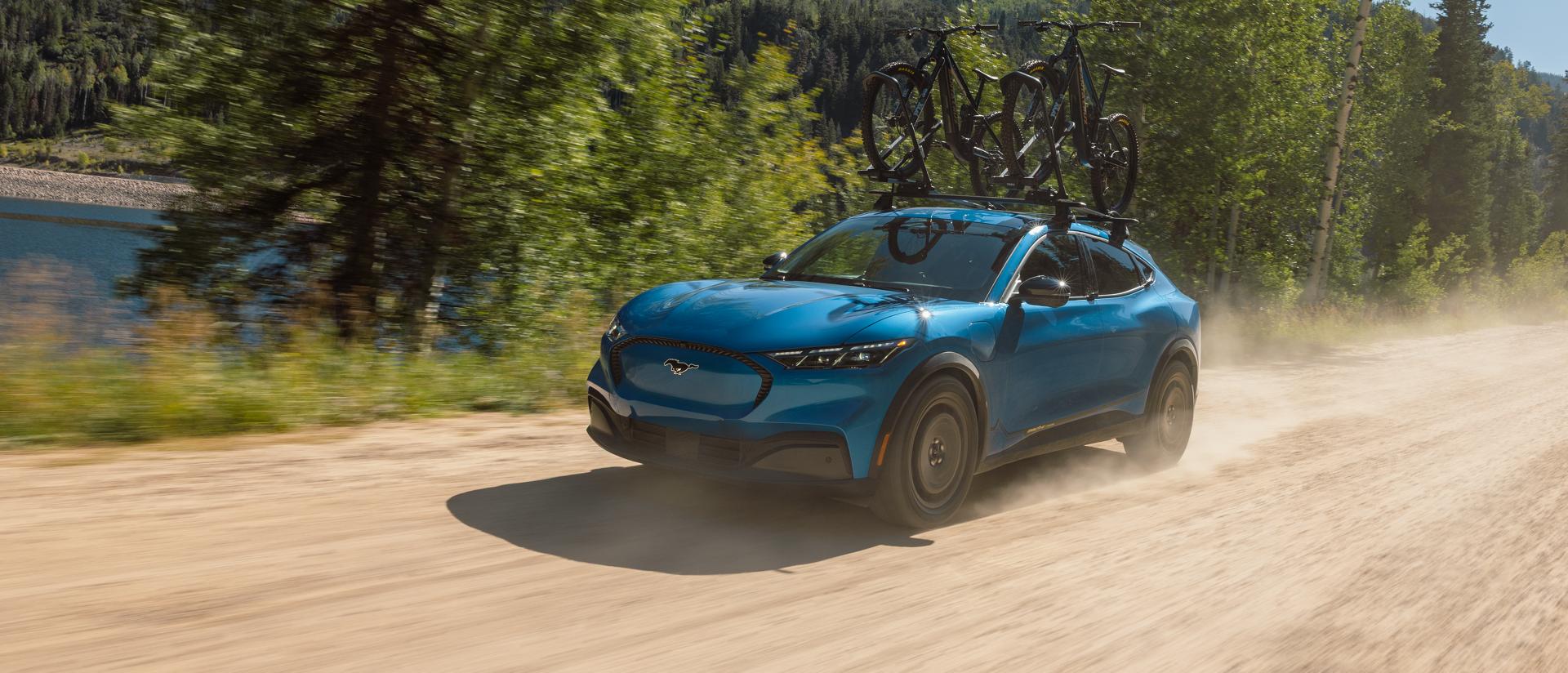 2027 Ford Mustang Mach-E® SUV with optional Trail package and available Ford bike rack accessory being driven on dirt road