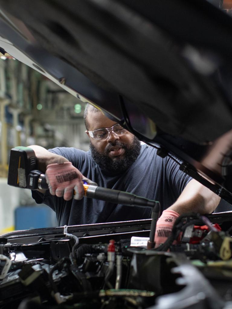 A Ford employee works under the hood of a Ford vehicle