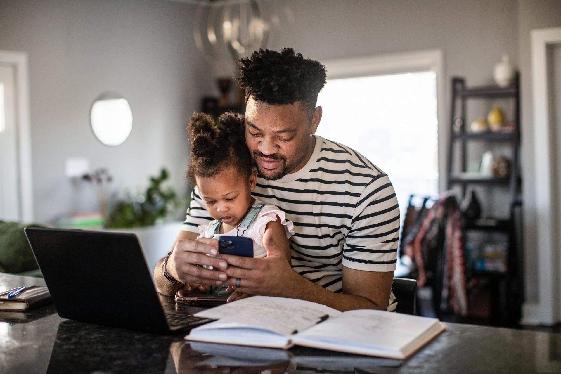 A father checks his phone with his daughter on his lap