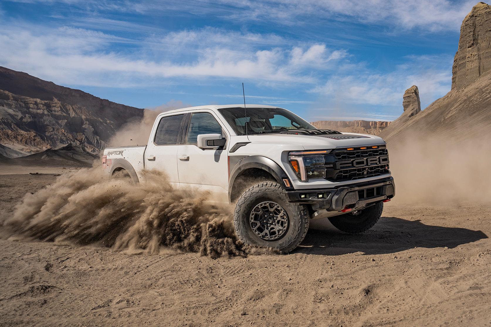 A white 2024 Ford F-150® Raptor® taking a turn in the desert, showcasing its daring design with a wide stance and flared fenders
