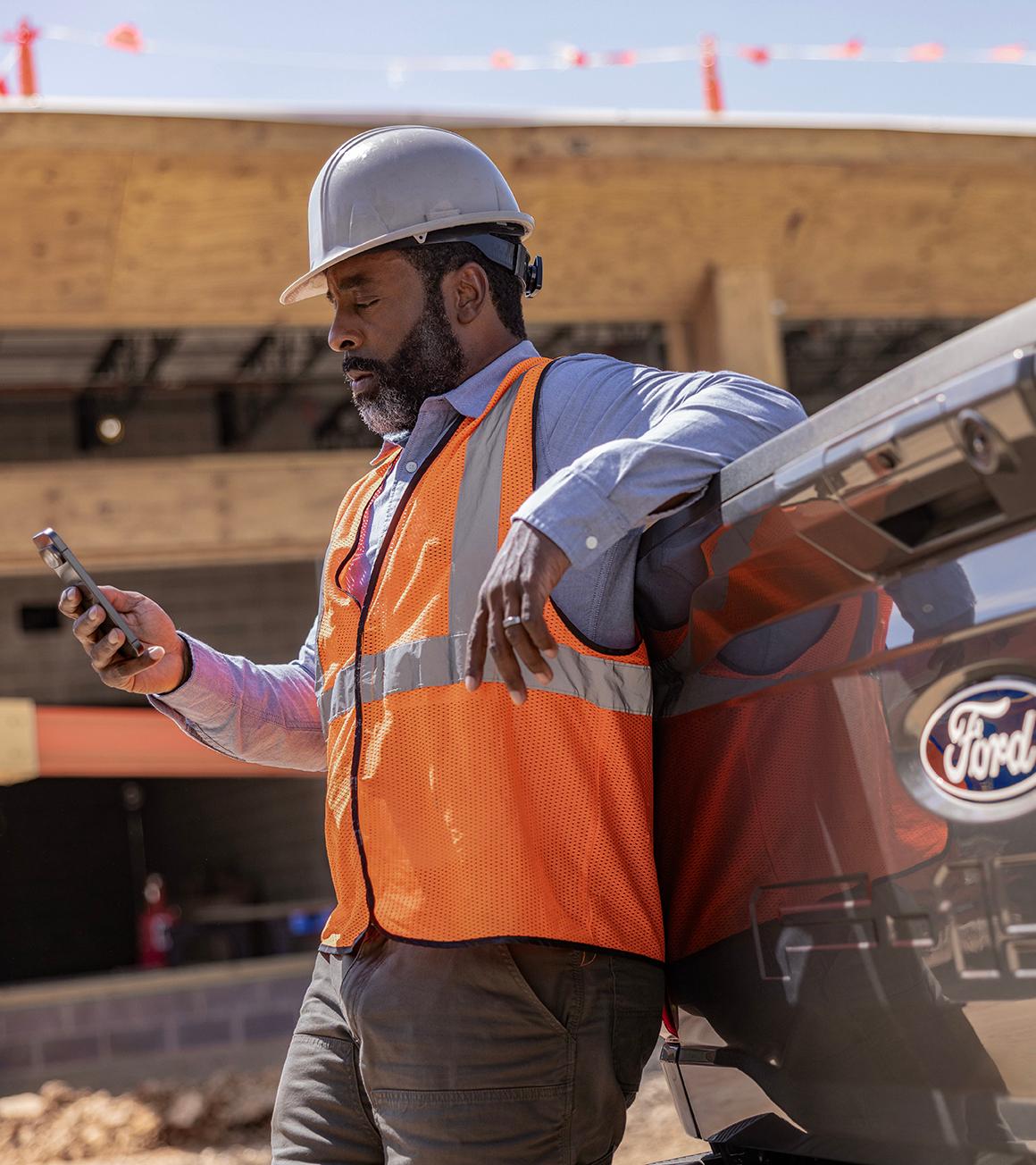 Construction worker looking at phone and leaning on the tailgate of a Ford truck