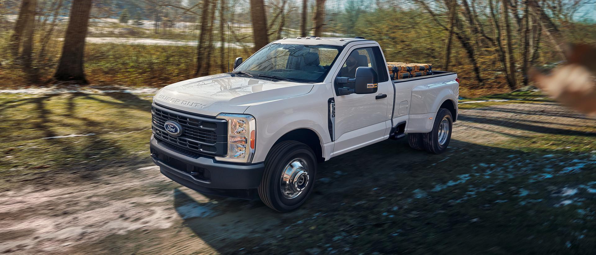 2026 Ford Super Duty® F-350® XL pickup driving on a dirt road with a full truck bed