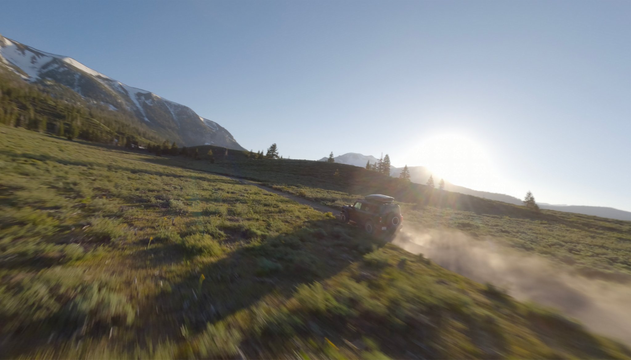 A 2026 Ford Bronco® SUV kicking up dust as it's driven through a grassy valley