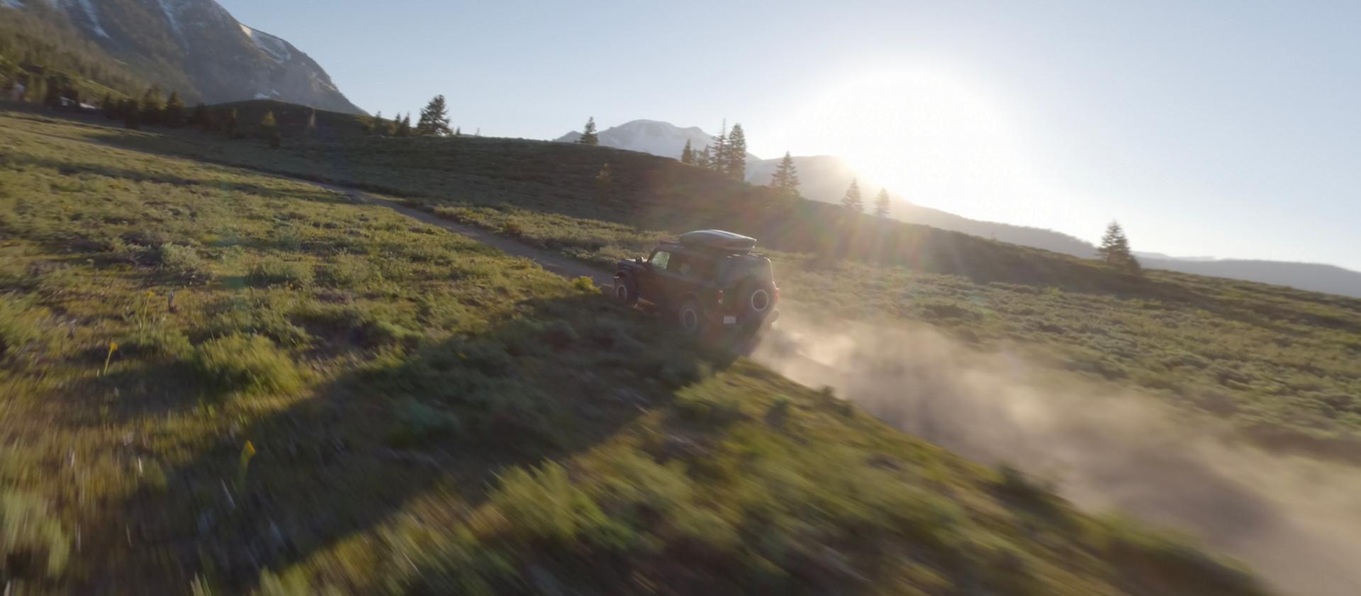 A 2026 Ford Bronco® SUV kicking up dust as it's driven through a grassy valley