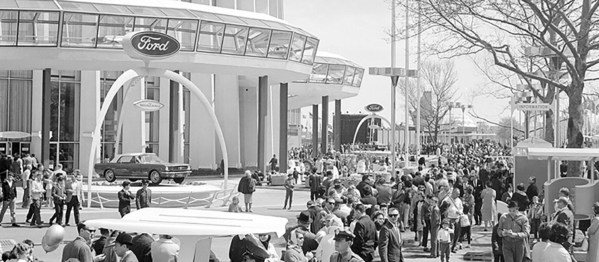 A black and white photo of many crowds standing outside a large building