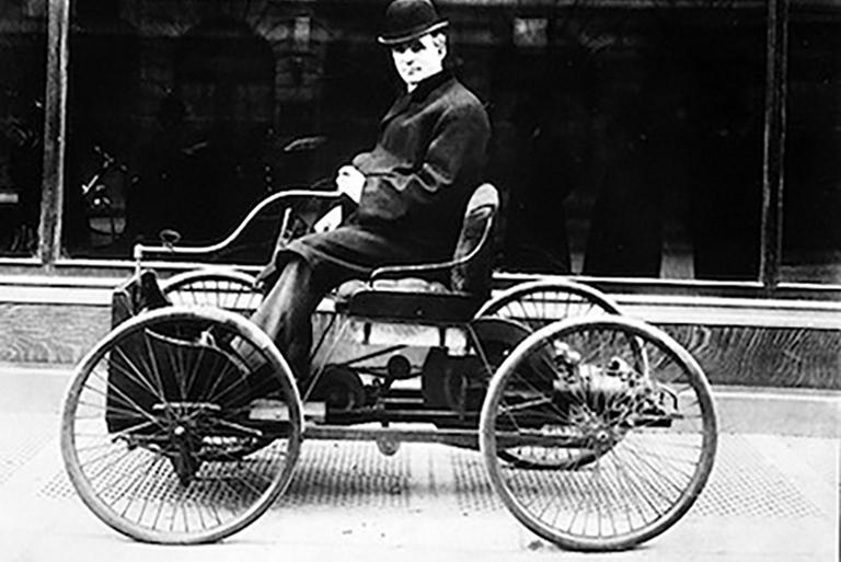 Henry Ford sits in the driver's seat of one of his first automobiles