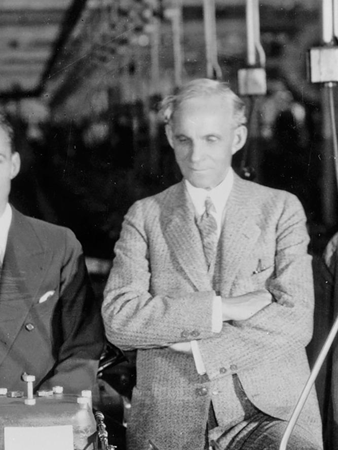 A black and white photo of Henry Ford lined up with executives inspecting a Model A engine