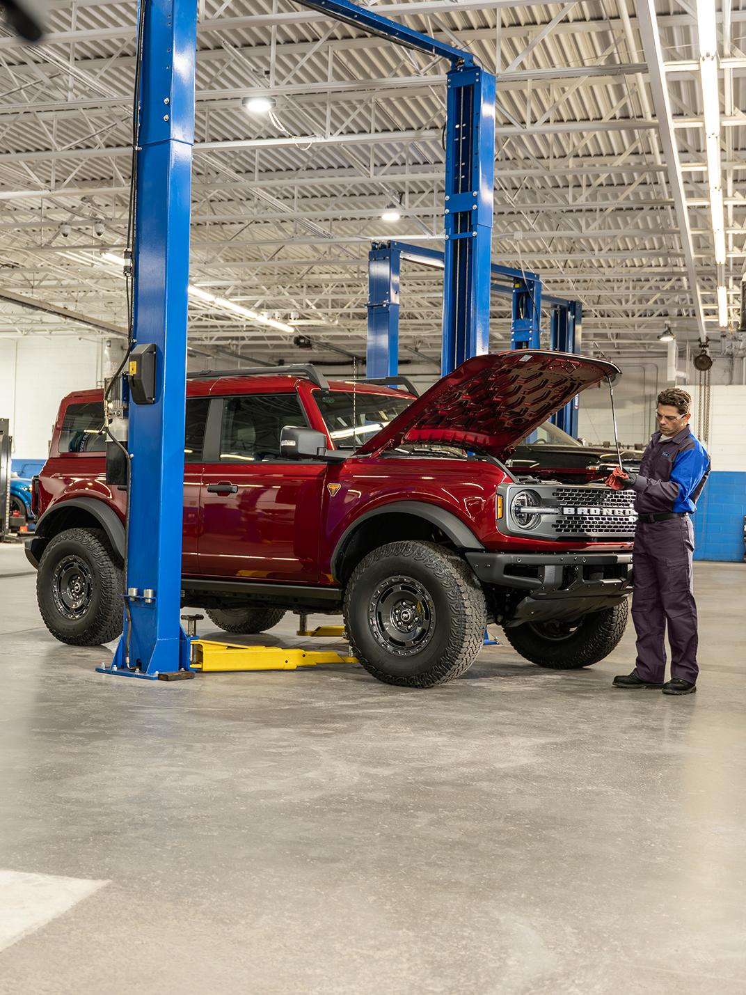A Ford Service technician works under the hood of a Ford Bronco® SUV in a service bay