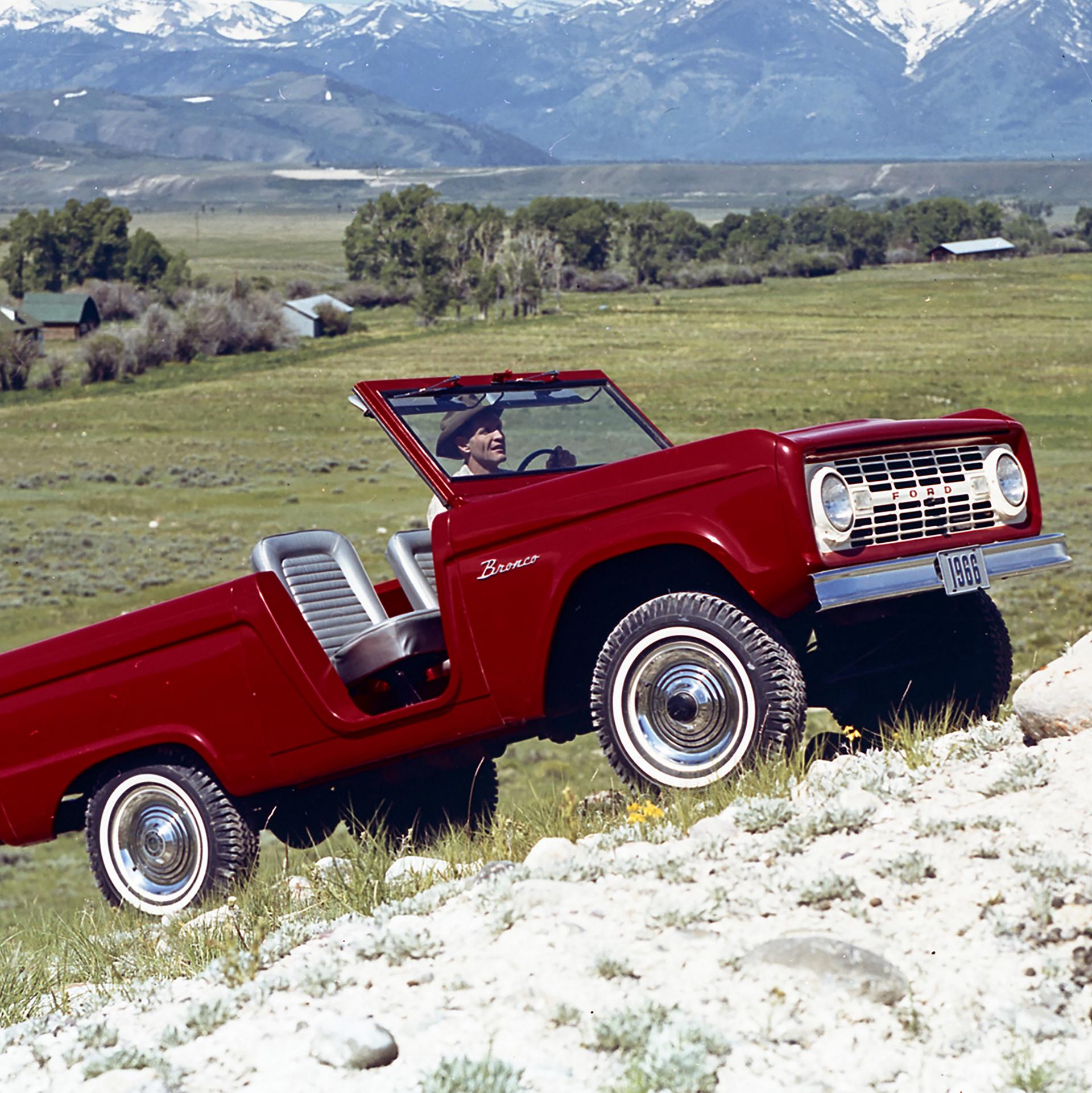 A 1966 Ford Bronco® model being driven up a rolling hillside
