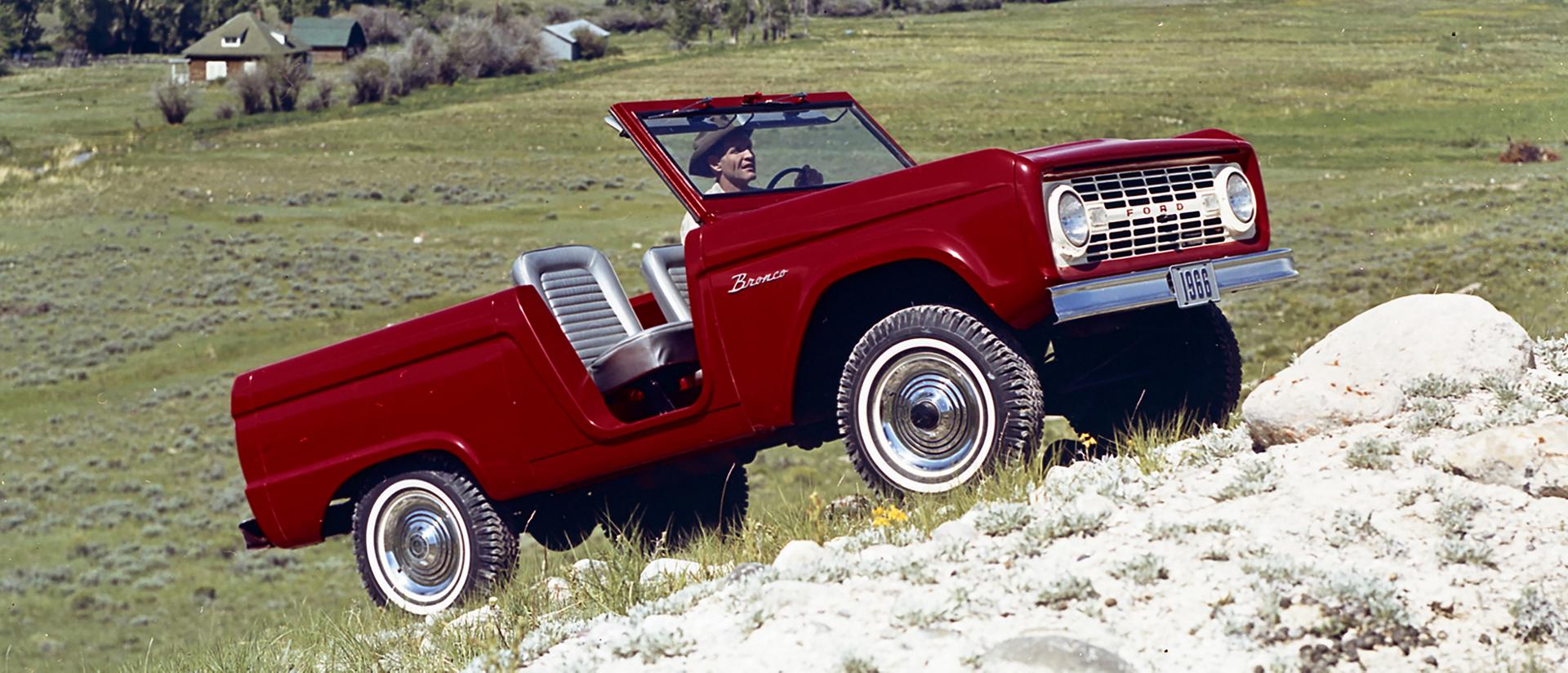 A 1966 Ford Bronco® model being driven up a rolling hillside