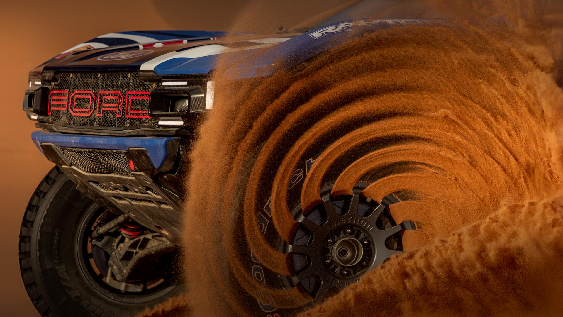 Ford Bronco Raptor racing through the desert with the front wheel spinning sand.