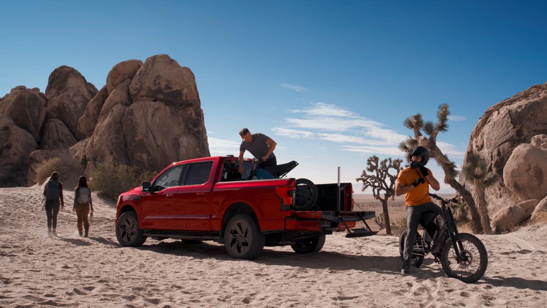 2025 Ford F-150® Lightning® pickup in the desert, with a dirtbike in the bed and one already unloaded