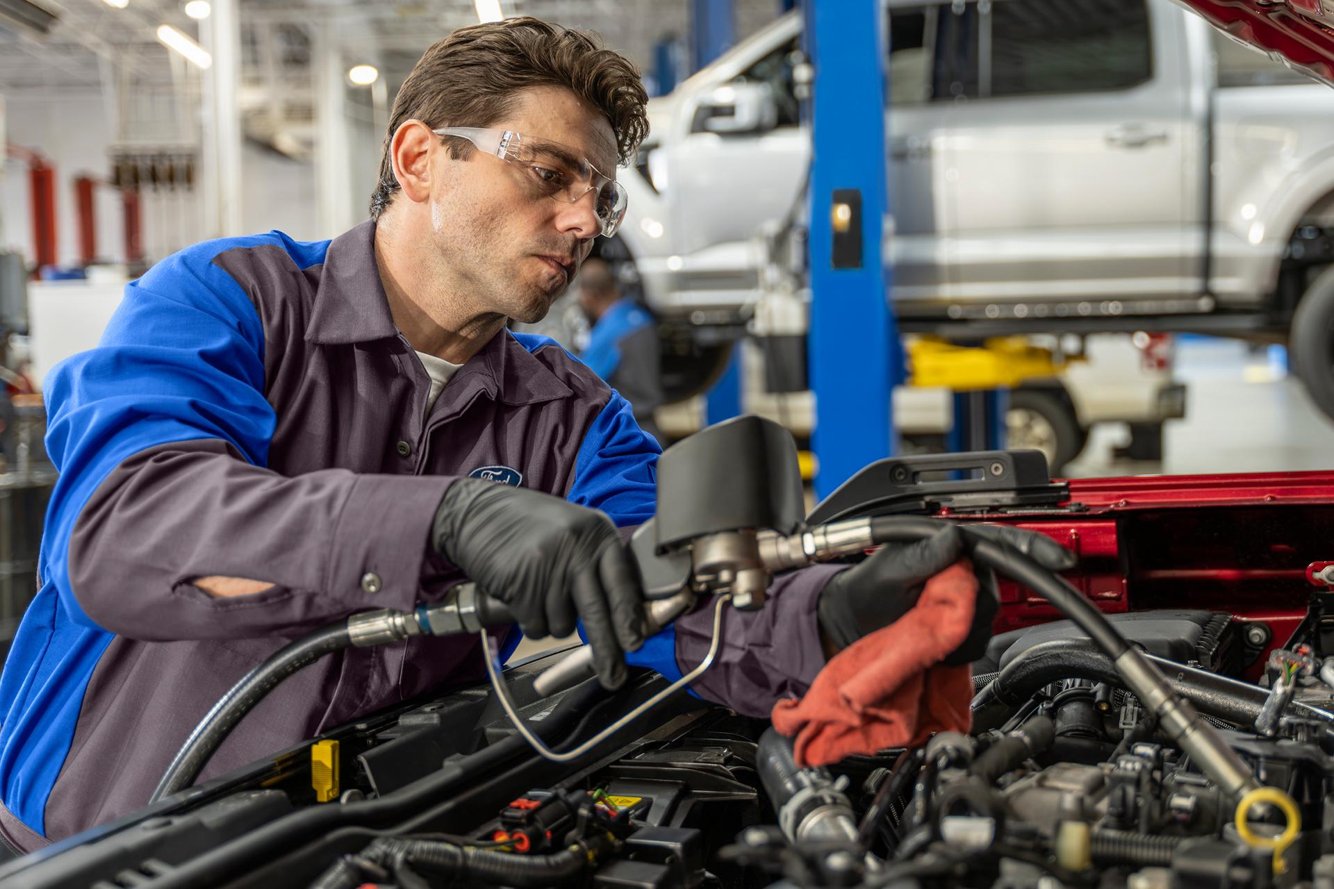 A Ford Service tech tops off fluid on a Ford vehicle