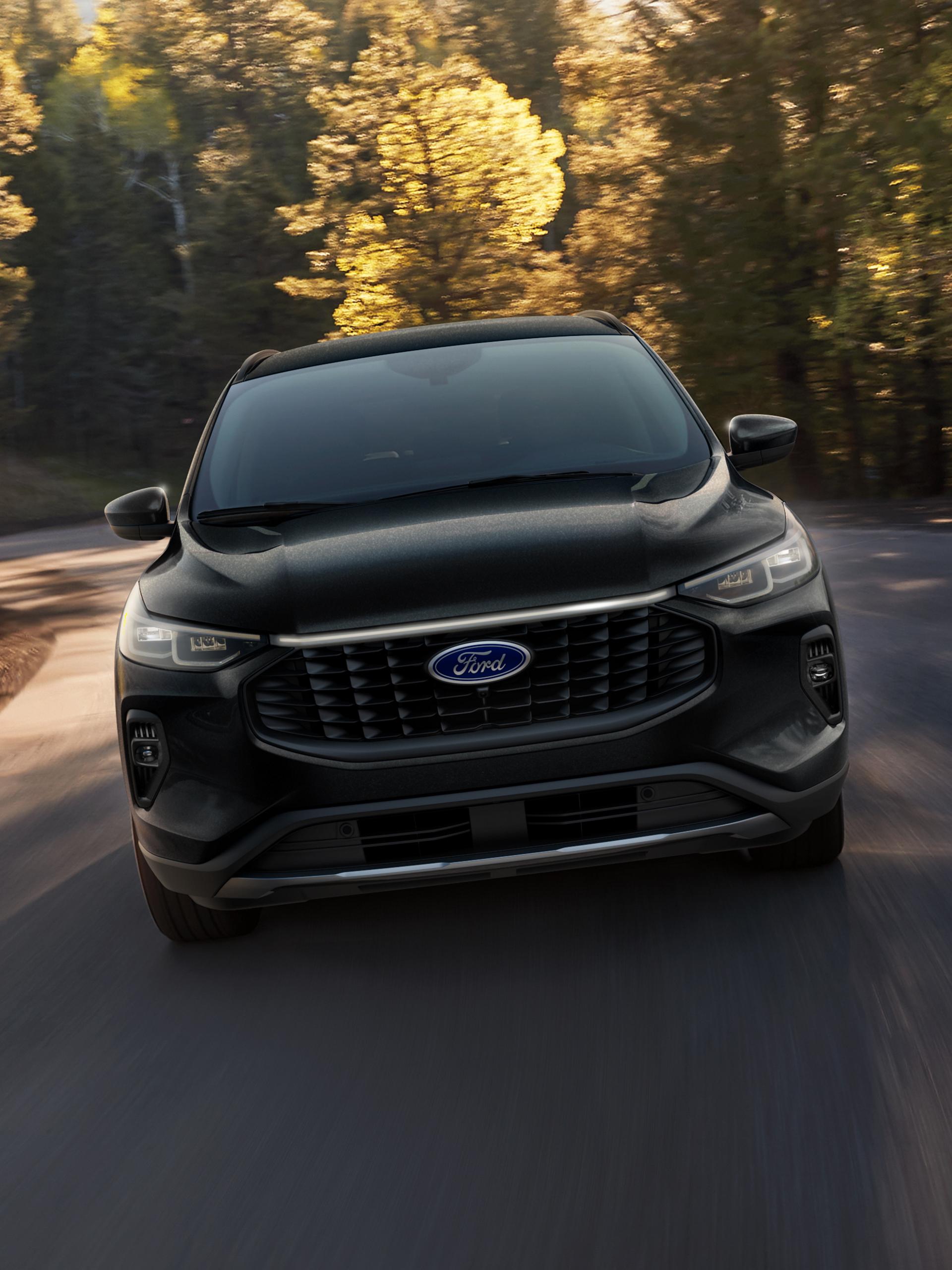 A 2024 Ford Escape® Plug-In hybrid model being driven on a tree-lined road
