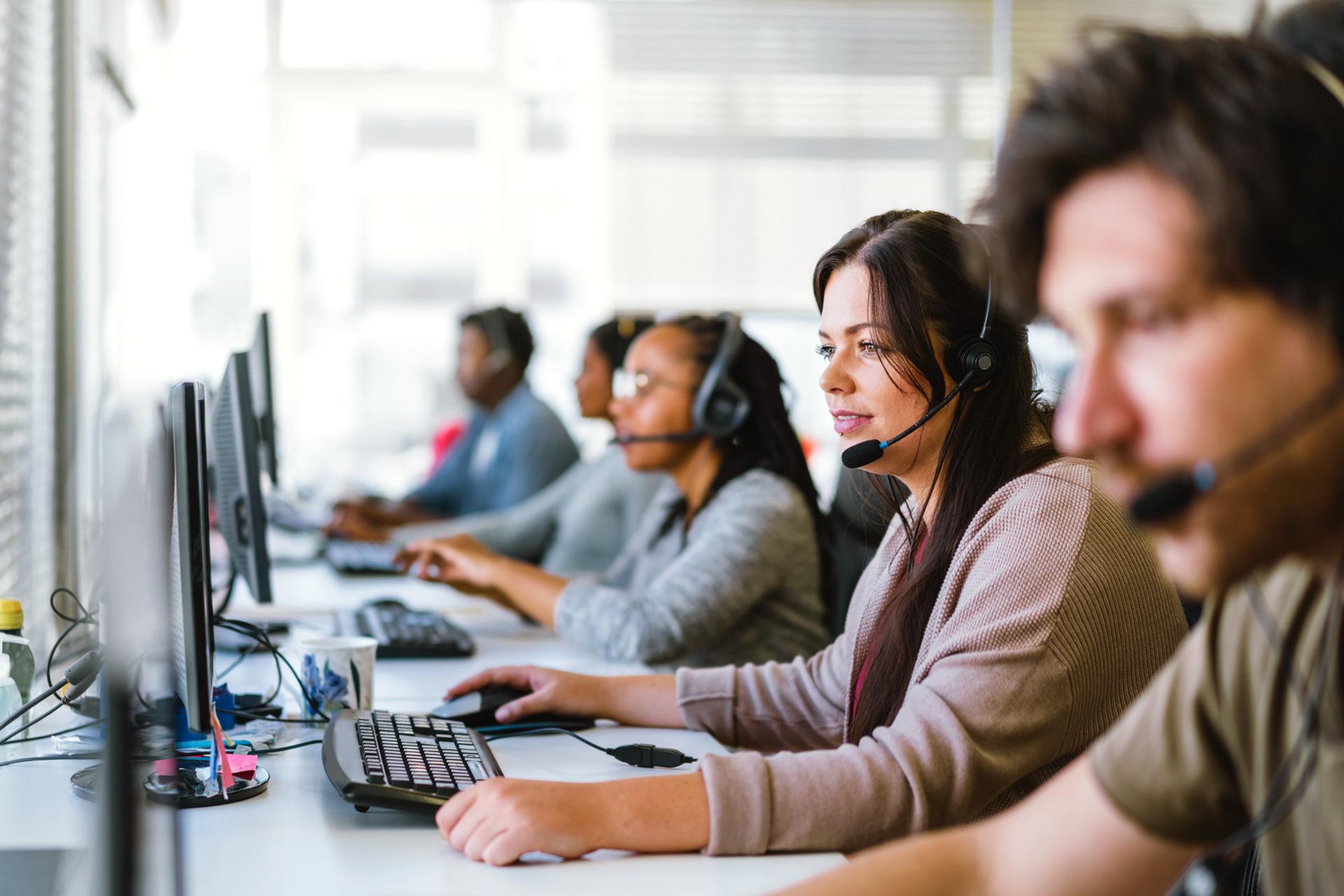 A team of customer service agents, all wearing headsets, seated at a row of computers