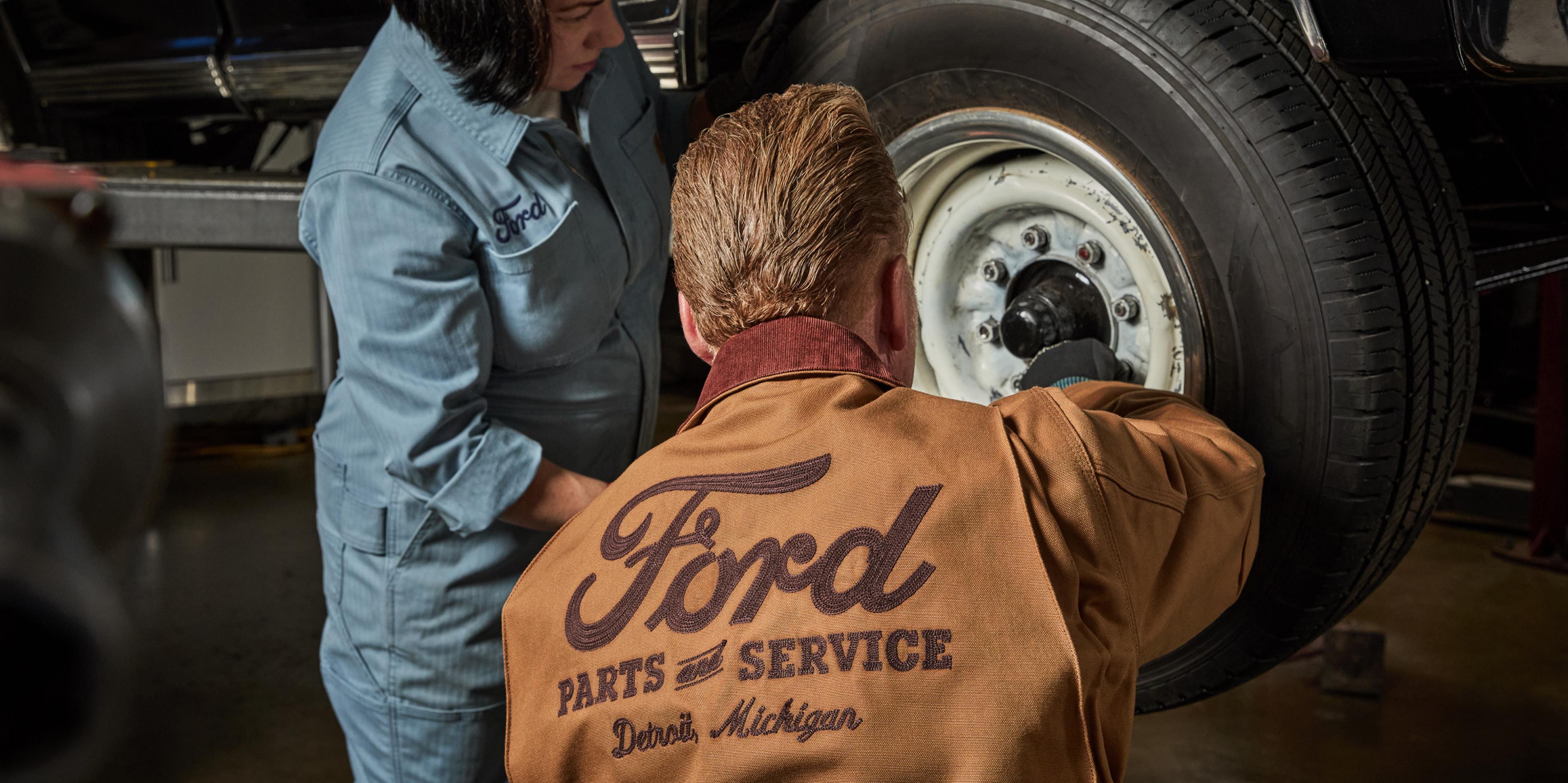 A person changing a tire while wearing a Carhartt® and Ford branded jacket