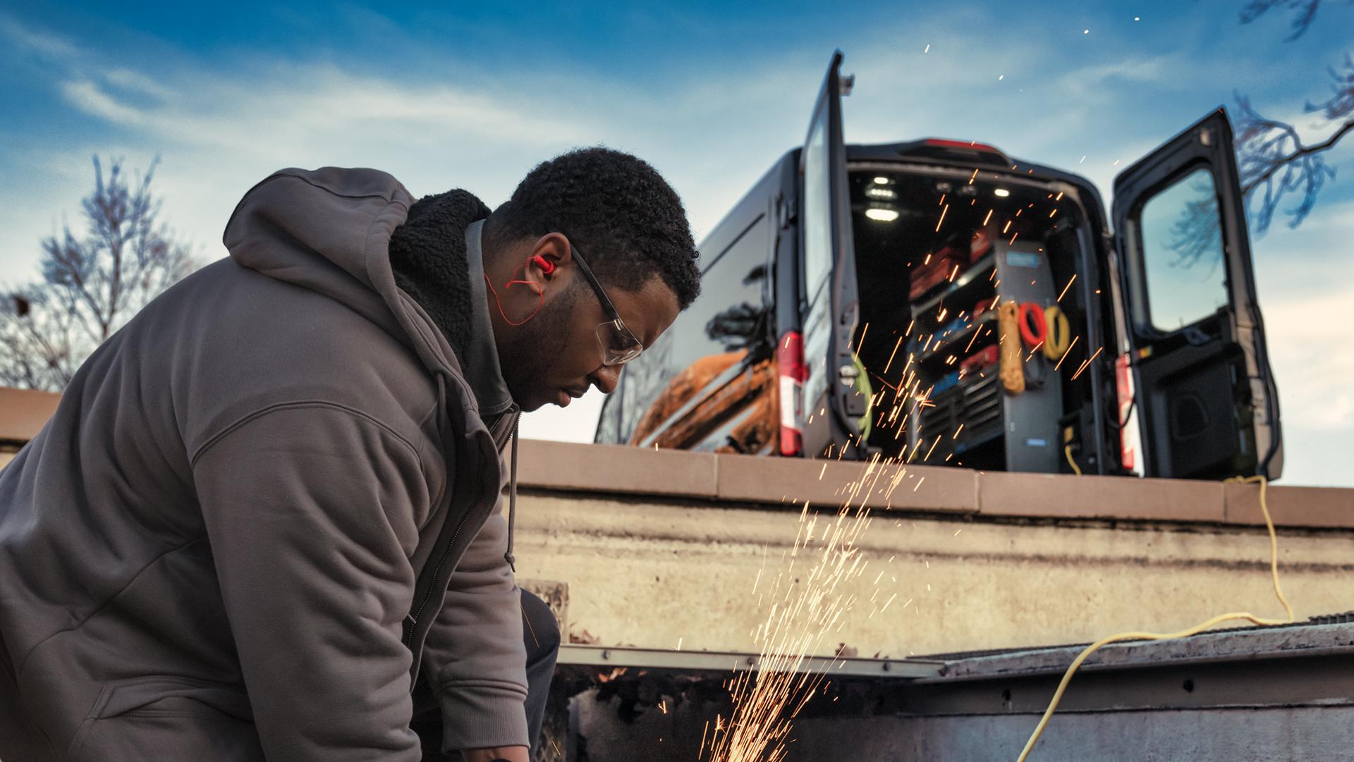 Close-up of a man using a power tool plugged into the Pro Power Onboard™ feature of a 2026 Ford E-Transit® Commercial Van
