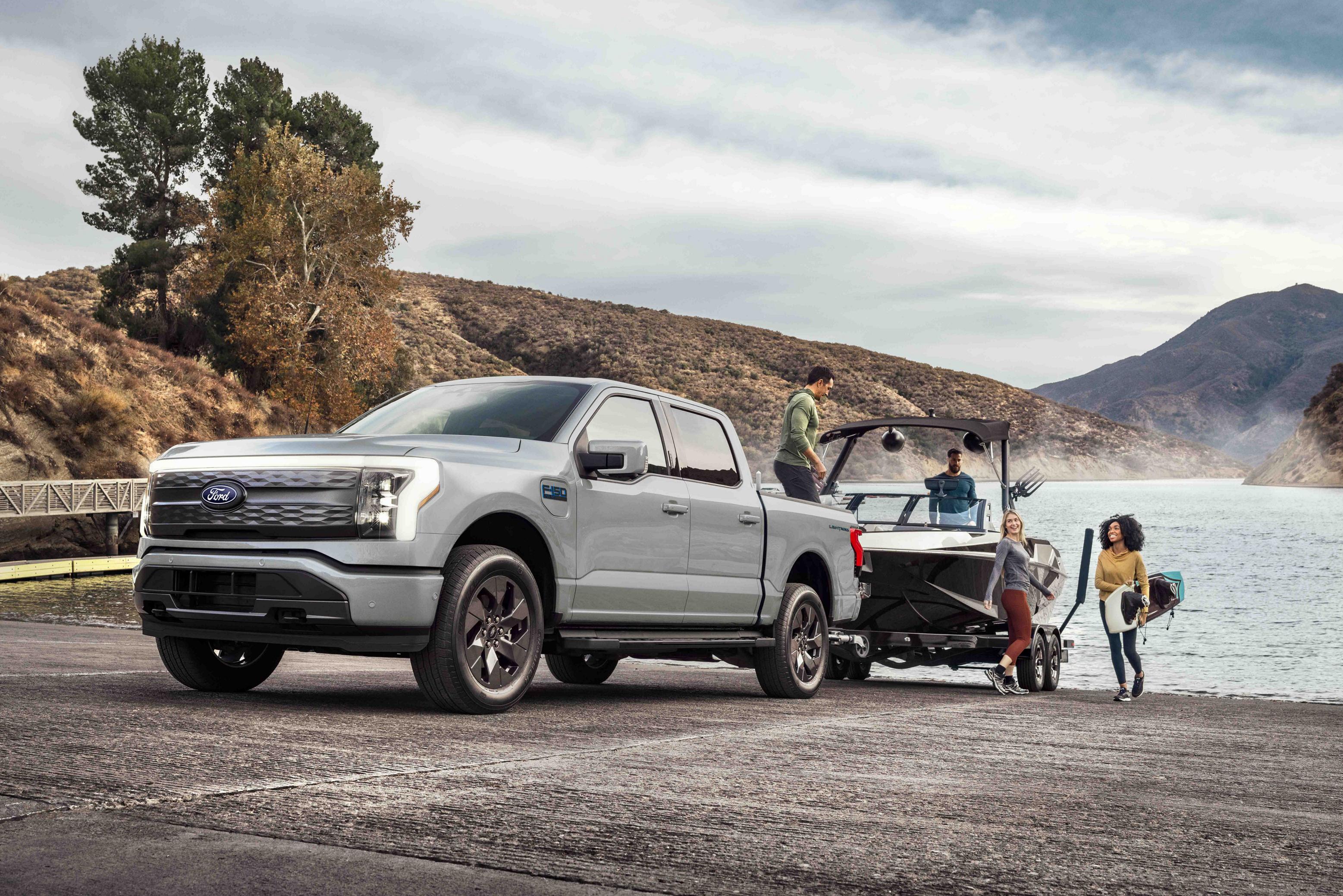 A 2025 Ford F-150® Lightning® pickup pulling a boat on a trailer out of a mountain lake