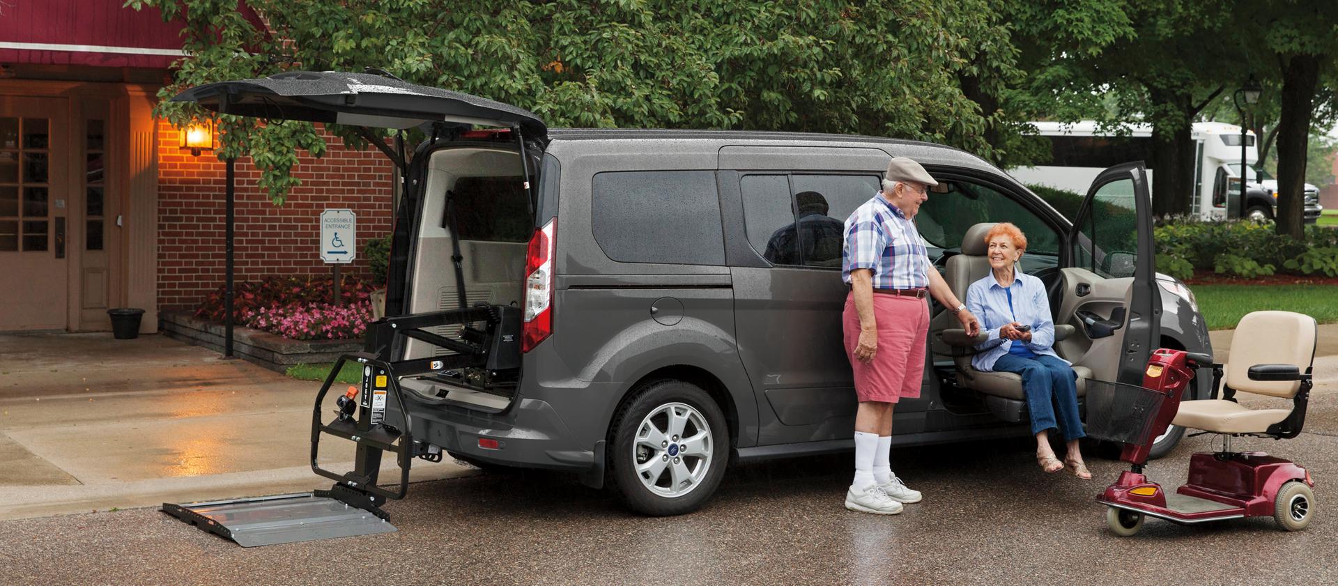 A man helping a woman out of a Ford vehicle, with a mobility scooter nearby