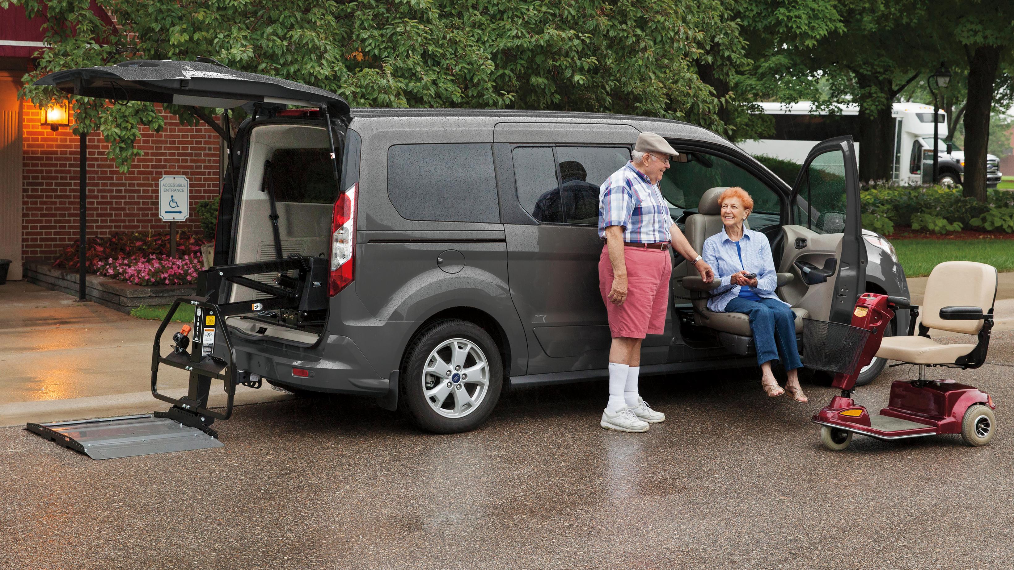 A man helping a woman out of a Ford vehicle, with a mobility scooter nearby