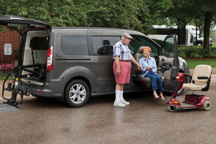 A man helping a woman out of a Ford vehicle, with a mobility scooter nearby